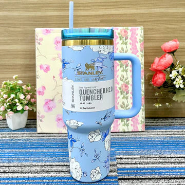 Floral-patterned Stanley tumbler on a striped surface with a floral box and flowers in the background.